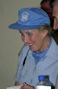 A profile picture of Margaret Anstee wearing a blue UN cap and light blue shirt. She is looking towards the left down and smiling to someone outside of the frame.
